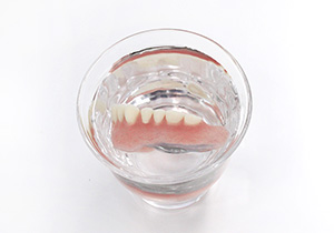 水とクリネが入ったグラスに義歯を入れる